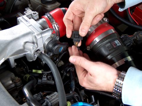 1996 Ford Probe - Hands disconnect a sensor from the engine's throttle body assembly, showing part of the intake system.