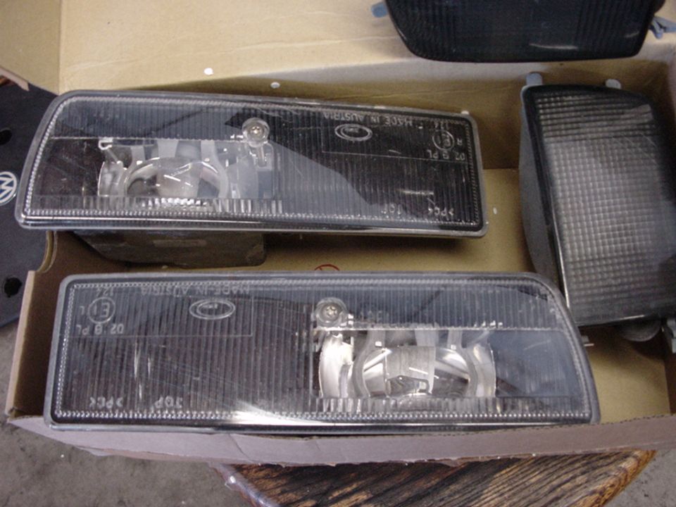 Two clear plastic car headlights with internal reflectors in a cardboard box