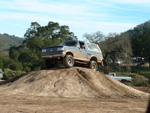 1991 Ford Bronco - A lifted Ford Bronco navigates a dirt mound during an off-road excursion.