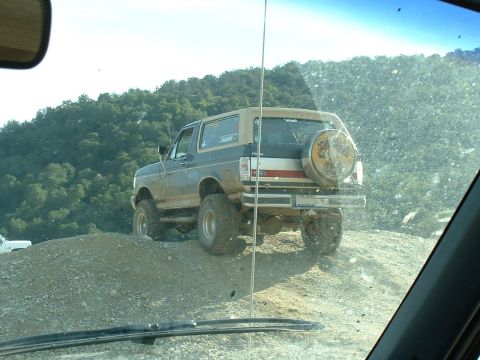 1991 Ford Bronco - This 1991 Ford Bronco is seen off-road, navigating a dirt incline with a spare tire mounted on the rear tailgate.