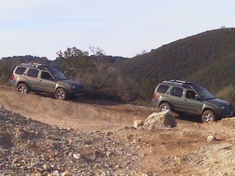 1991 Ford Bronco - Two Nissan Xterras navigate a rocky, off-road trail under a clear sky.