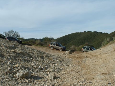 1991 Ford Bronco - Multiple SUVs navigate a challenging dirt path under a partly cloudy sky.