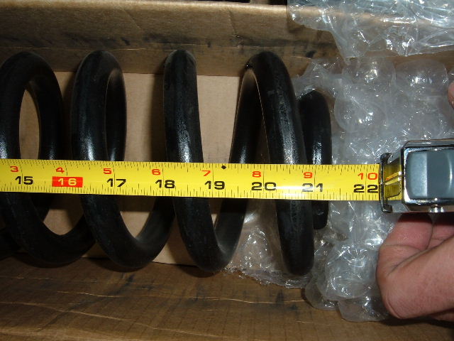 Black coil spring in cardboard box measured with yellow tape measure showing about 15 to 22 inches