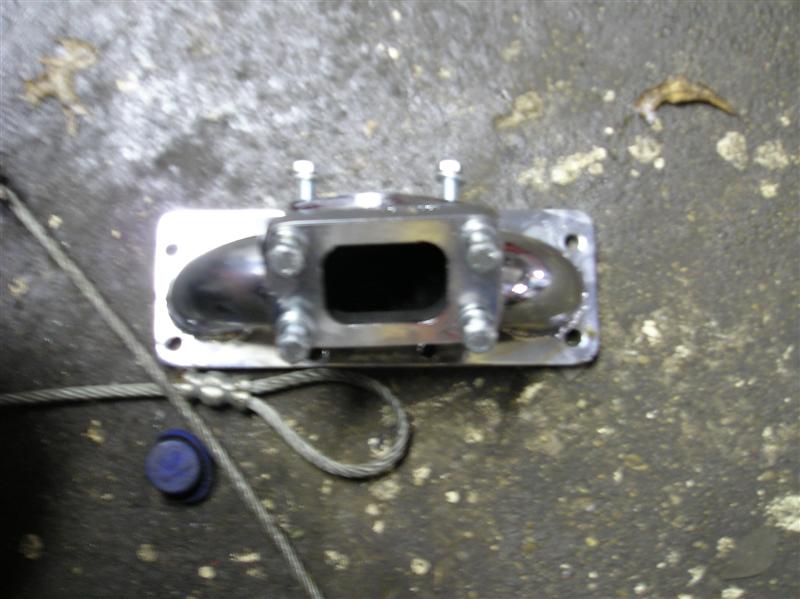 Metal exhaust manifold part with bolts on a concrete surface