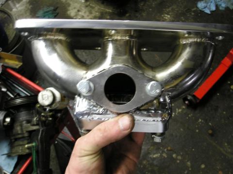 1994 Ford Probe - A custom exhaust manifold is held in hand, showing its polished metal construction and bolted flange.