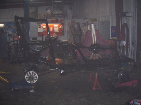 1999 Jeep TJ - Vehicle frame and suspension parts are visible in a workshop setting, supported by jack stands.