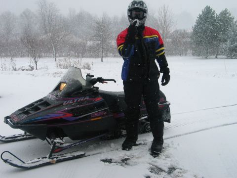 1990 Ford Mustang - A person in winter clothing stands beside a snowmobile during a snowfall.