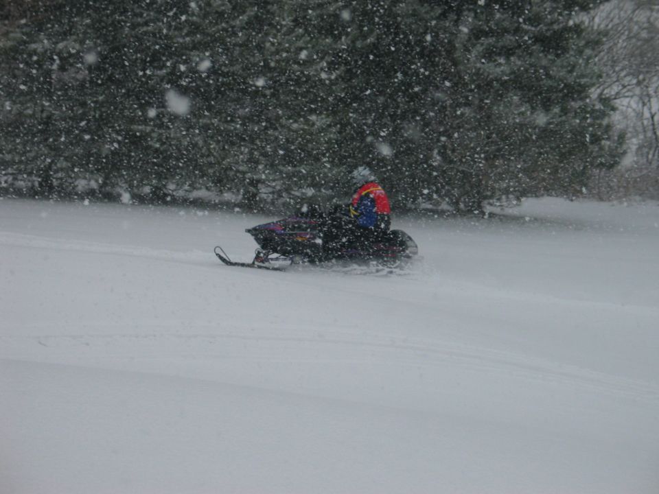 Snowmobile with rider in colorful jacket moving through falling snow