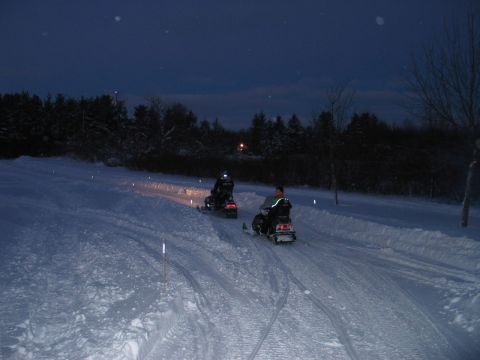 1990 Ford Mustang - Two snowmobiles travel along a marked trail through a snowy landscape as twilight deepens.