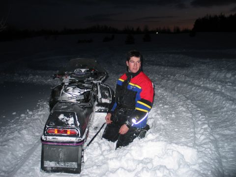 1990 Ford Mustang - A person kneels next to a snowmobile in a snowy landscape at dusk.