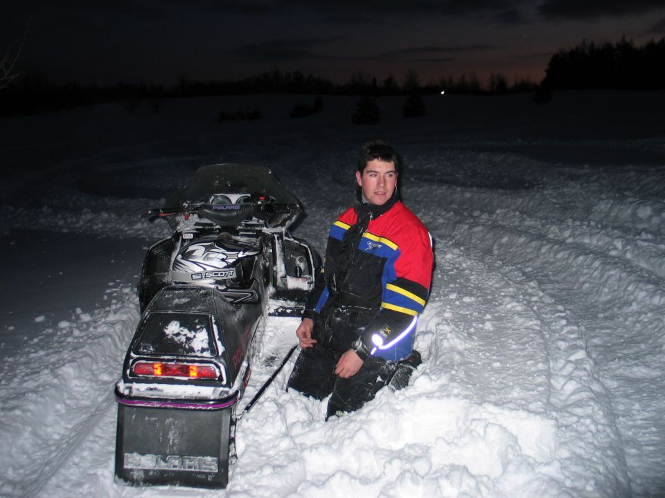 Snowmobile in snow with a person kneeling beside it
