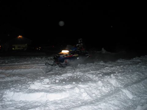 1990 Ford Mustang - A snowmobile travels through the snow at night, with a building visible in the distance.