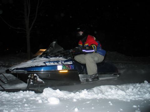 1990 Ford Mustang - A person rides a blue snowmobile through the snow at night, with the license plate 5653PF visible.
