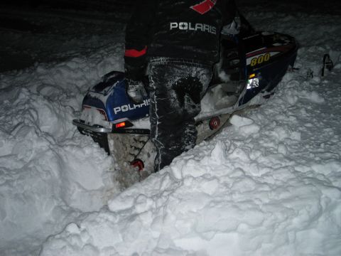1990 Ford Mustang - A Polaris snowmobile is stuck in a large snowdrift, with a person in a Polaris jacket nearby.