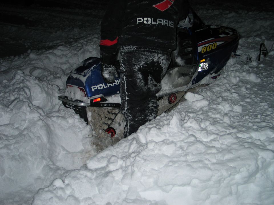 Polaris snowmobile stuck in deep snow, person in Polaris jacket standing next to it