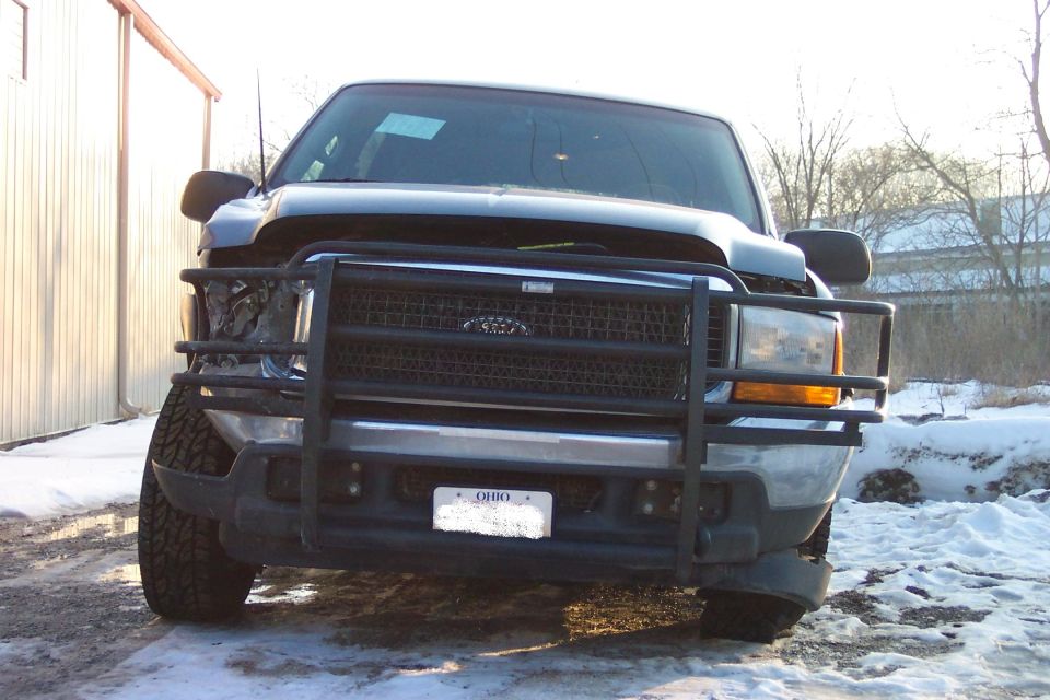 Front of dark Ford SUV with black grille guard, damaged left front corner, Ohio plate, parked in snow.