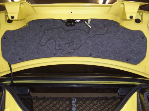 2002 Ford Mustang - The trunk interior of a yellow 2002 Ford Mustang features a carpeted panel with an embossed running horse logo.