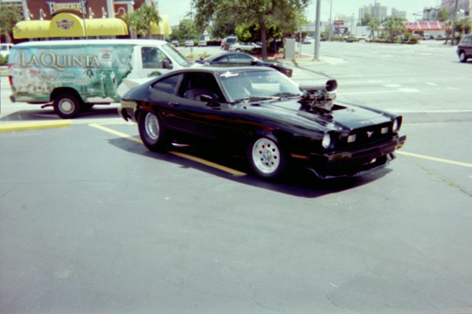 Black Mustang II hatchback with blower scoop through the hood in a parking lot