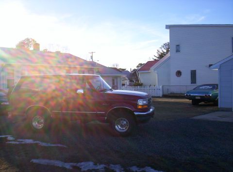 1995 Ford Bronco - A red 1995 Ford Bronco is parked in a driveway next to a house, with another car visible in the background.