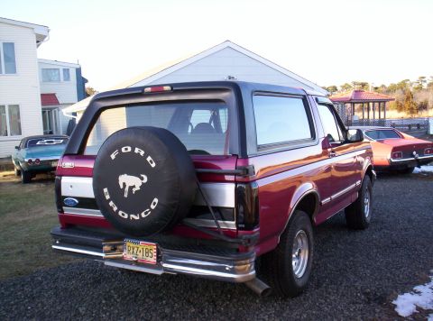 1995 Ford Bronco - Maroon Ford Bronco from the 1990s parked outside with another vehicle in the background.