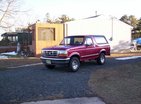 1995 Ford Bronco - This 1995 Ford Bronco is parked in a driveway with a house and wooden structure in the background.