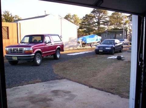 1995 Ford Bronco - A maroon Ford Bronco is parked outside a building next to other vehicles and a boat on a trailer.