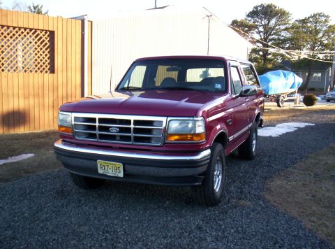 1995 Ford Bronco - This Ford Bronco is parked outside next to a wooden fence with a boat on a trailer in the background.