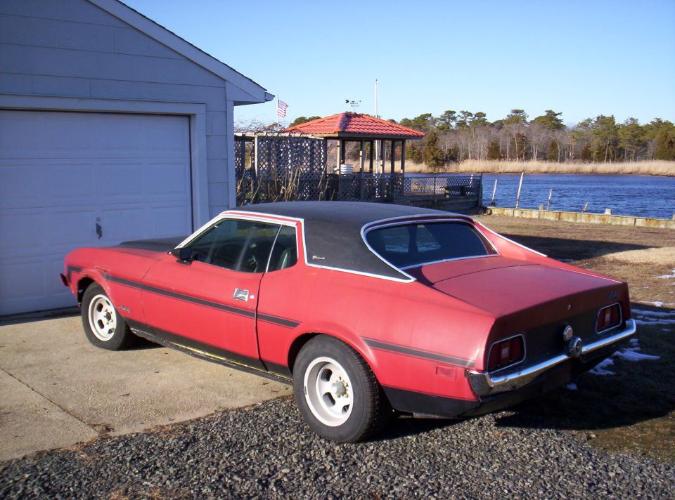 Red 1973 Ford Mustang coupe parked by a garage near water