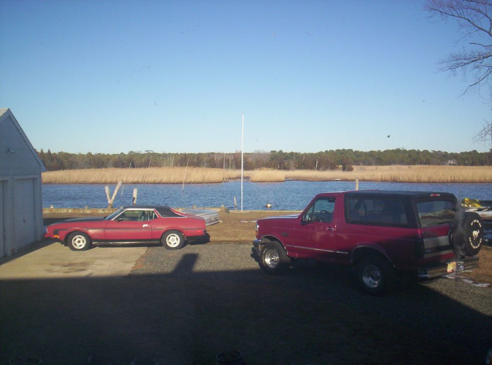 Red 1971 Ford Mustang coupe and red Ford Bronco parked by a body of water