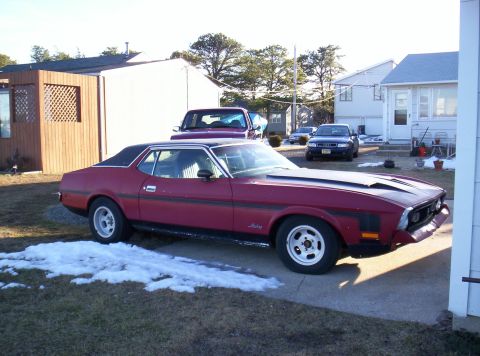 1971 Ford Mustang - Maroon 1971 Ford Mustang coupe with black accents and hood scoops sits in a driveway with snow patches.