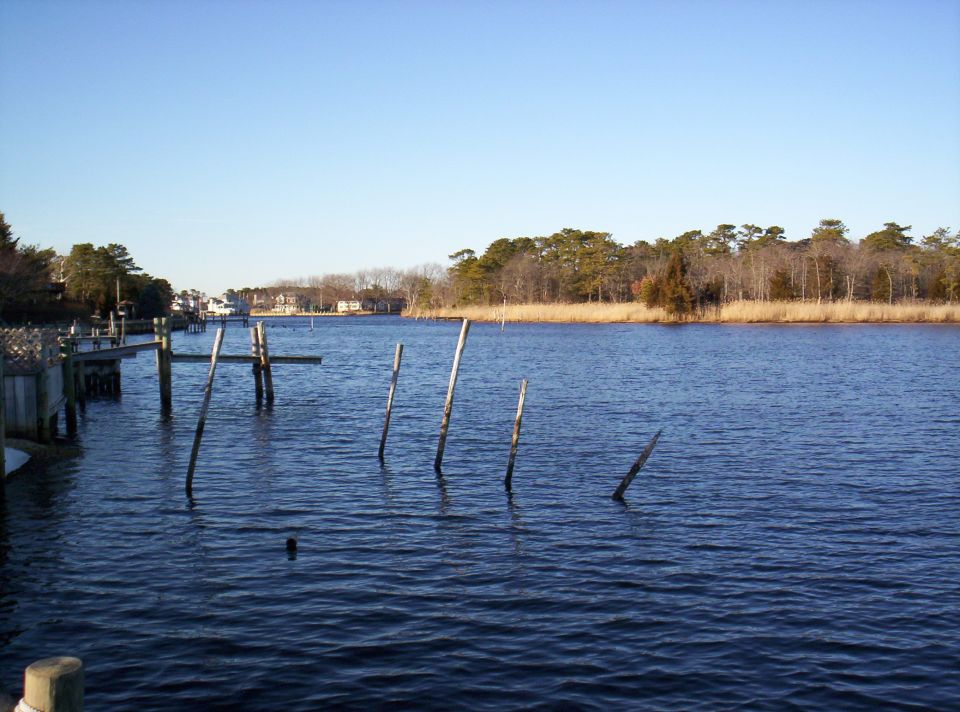 Waterway with wooden docks and pilings, trees line the distant shore under a clear blue sky