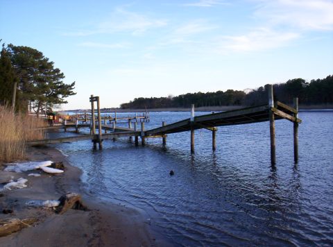 1995 Ford Bronco - A long wooden dock stretches out over the calm blue water, with trees lining the distant shore.