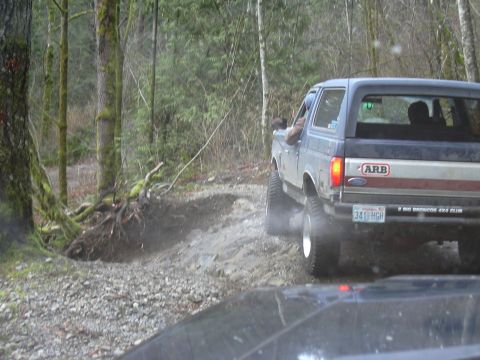 1991 Ford Bronco - A blue 1991 Ford Bronco navigates a wooded trail, kicking up dust from its tires.