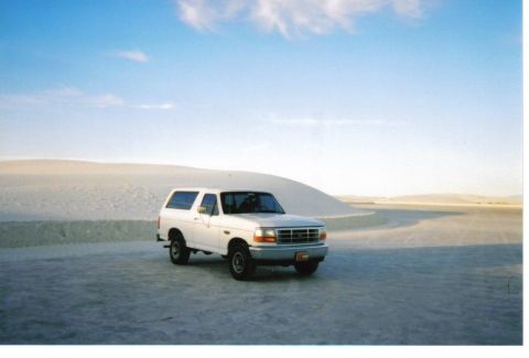 1996 Ford Bronco - A white SUV is parked in a desert landscape under a blue sky with scattered clouds.