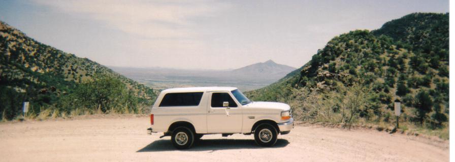 White 1996 Ford Bronco side view parked on a dirt road in a mountainous landscape