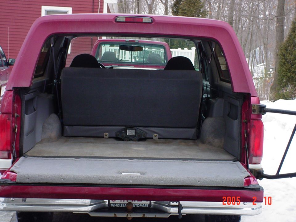 Maroon Ford Bronco rear interior with folded down seats and a red pickup truck visible through the open tailgate