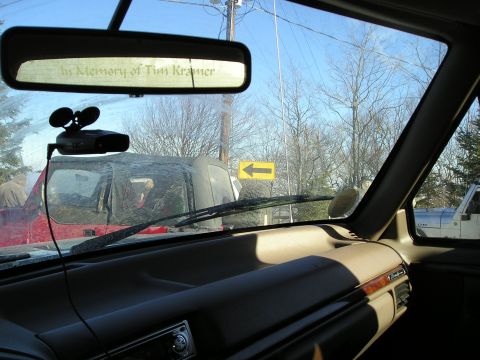 1996 Ford Bronco - View from inside a vehicle shows a red SUV and a white Jeep, with a radar detector mounted and a memorial message on the rearview mirror.