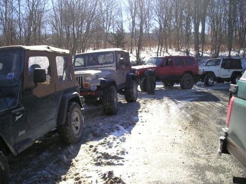1996 Ford Bronco - A line of off-road vehicles, including Jeeps and a red SUV, are parked on a dirt road covered in snow and mud.