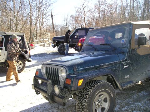1996 Ford Bronco - A group of off-road vehicles, including a green Jeep Wrangler and a black truck, are parked in a snowy, wooded area.