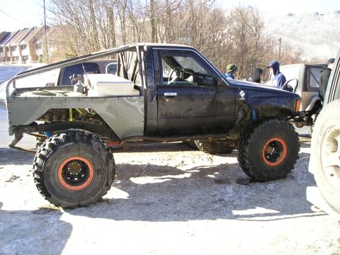1996 Ford Bronco - A heavily modified pickup truck with oversized tires and a custom roll cage is parked outdoors on a sunny day.