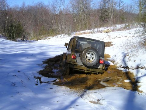 1996 Ford Bronco - A Jeep Wrangler is stuck in a muddy ditch on a snowy day.