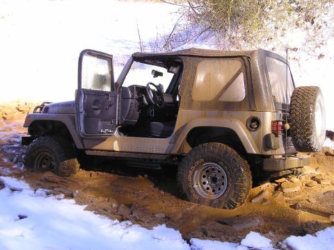 1996 Ford Bronco - A tan Jeep Wrangler is stuck in thick mud with its doors open, surrounded by snow and dirt.