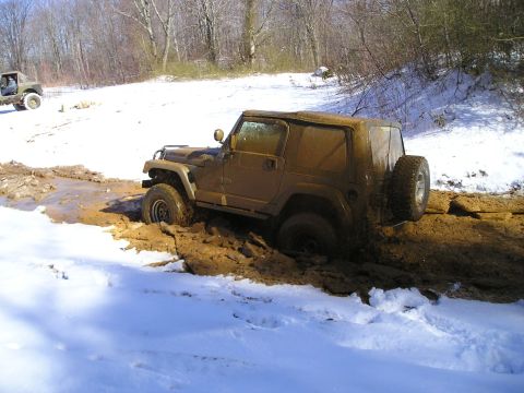 1996 Ford Bronco - A muddy Jeep Wrangler struggles in a snowy, off-road environment, while another vehicle is visible in the distance.