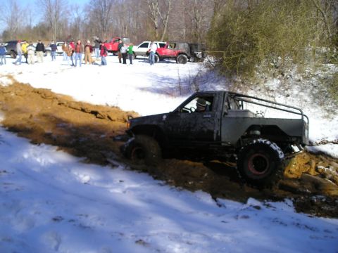 1996 Ford Bronco - A group of people watch as a modified truck attempts to navigate a muddy, snow-covered trail.