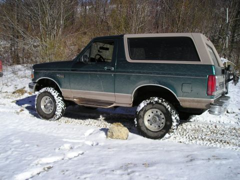 1996 Ford Bronco - A green 1996 Ford Bronco with a tan top is parked in a snowy landscape.
