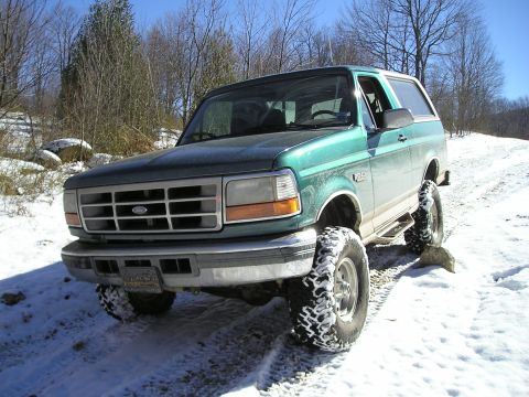 1996 Ford Bronco - A green Ford Bronco is parked on a snowy trail with trees in the background.