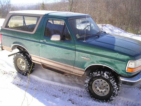 1996 Ford Bronco - A green 1996 Ford Bronco with tan trim is shown from a 3/4 front angle in a snowy environment.