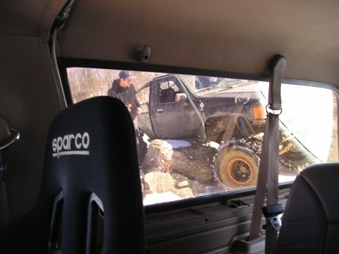 1996 Ford Bronco - View from inside a vehicle shows a black pickup truck struggling over a rocky, snow-covered terrain.