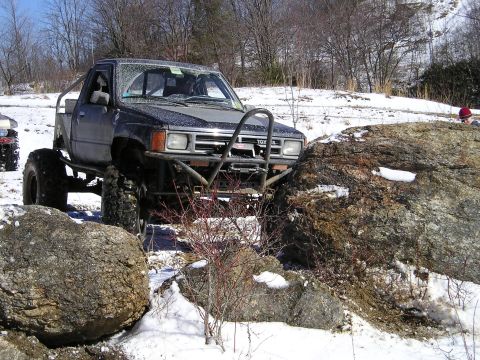 1996 Ford Bronco - Modified Toyota pickup truck off-roading over rocks in a snowy environment.