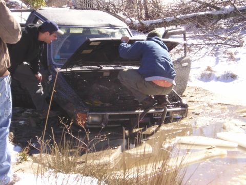 1996 Ford Bronco - Two men inspect the engine of a stuck Toyota truck in a muddy, icy environment.